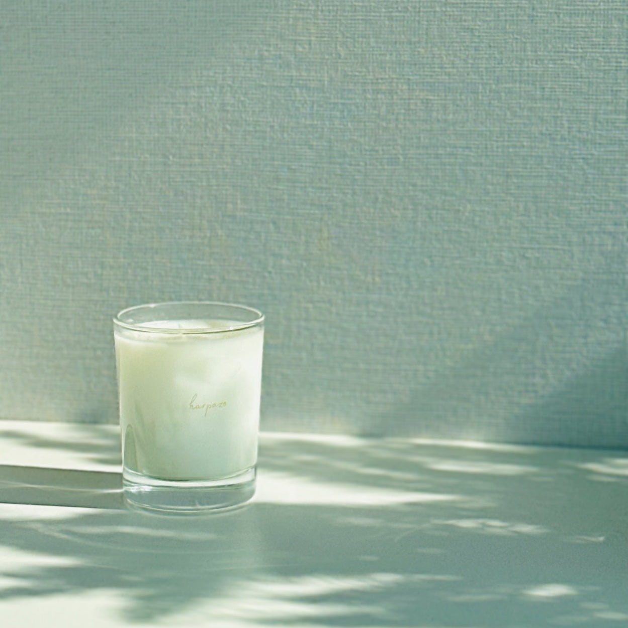 A white aromatic candle in a clear glass holder, placed on a surface with a textured background.