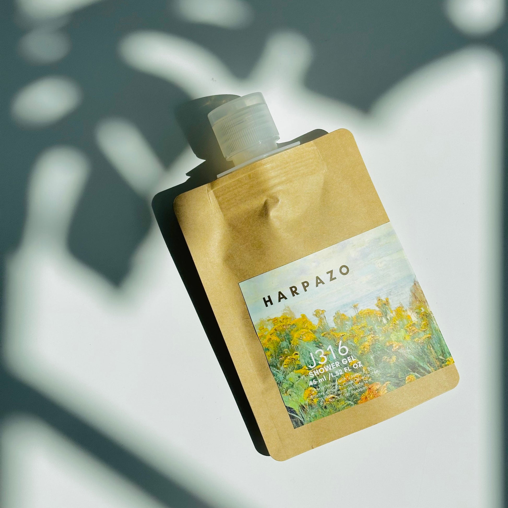Travel size shower gel bottle with a beige to brown gradient color and a label featuring green and yellow tones, set against a shadowed background.