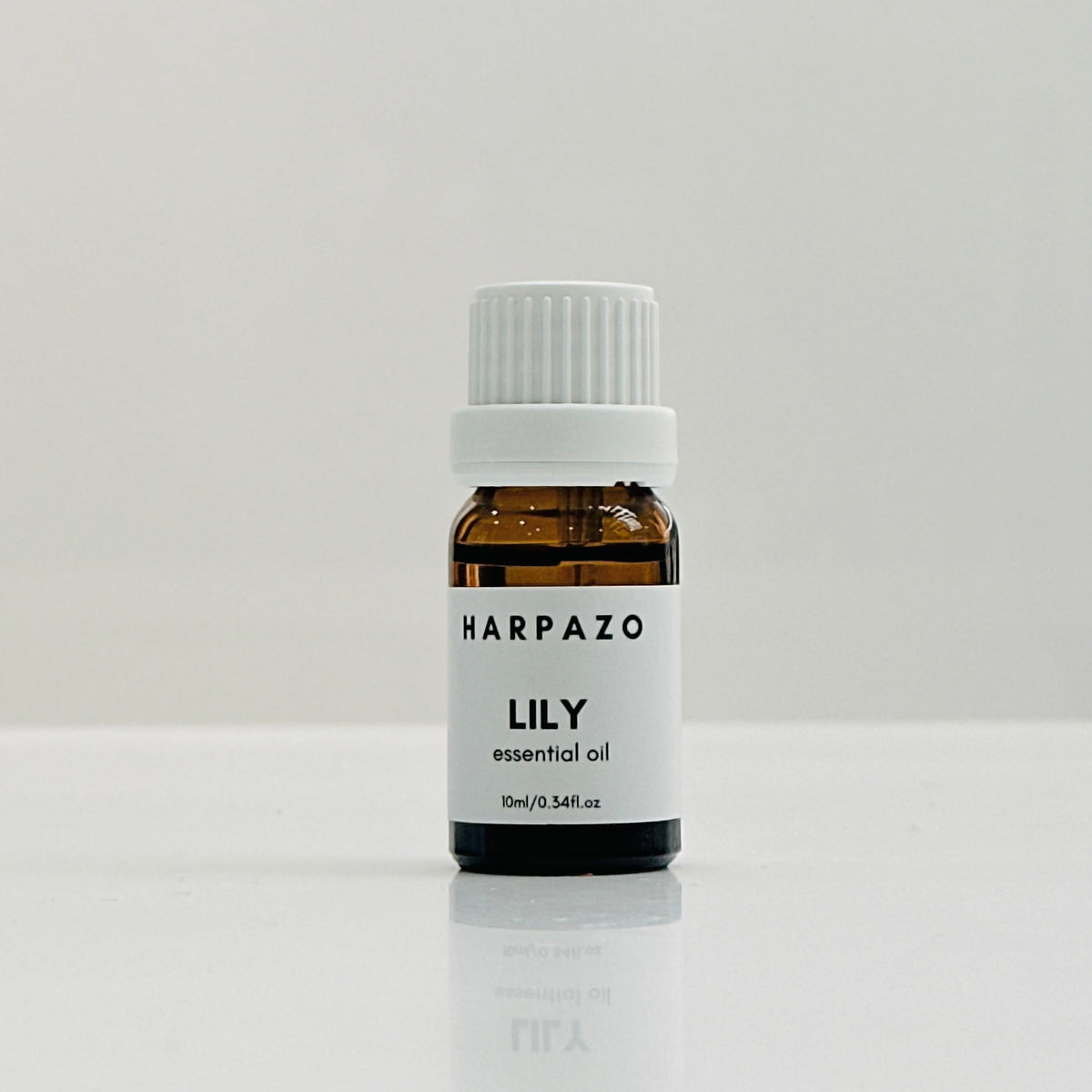 A small bottle labeled 'HARPAZO LILY essential oil' with a white cap, placed on a white surface.