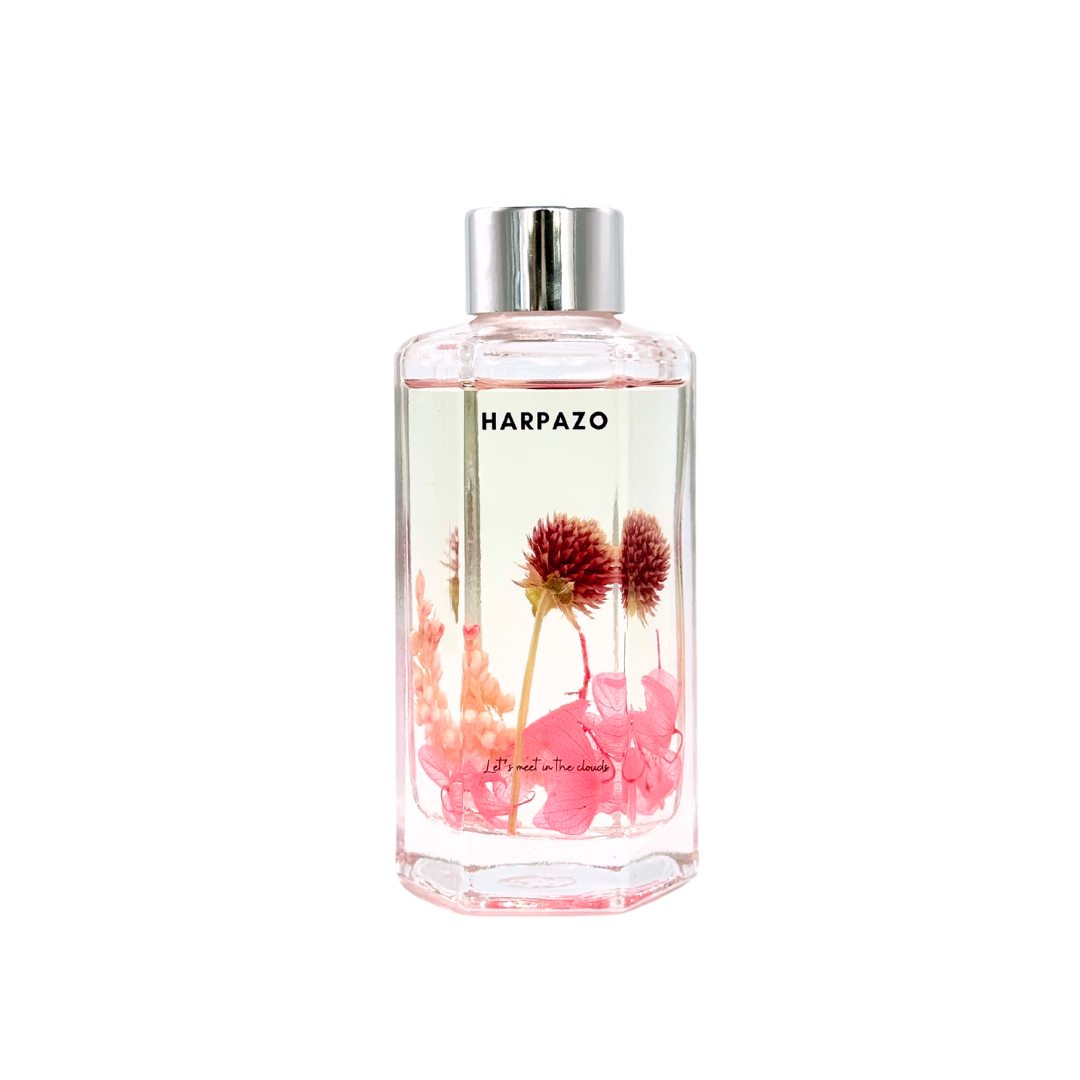 A clear glass reed diffuser bottle with pink floral elements and the brand name 'HARPAZO' visible on the label.