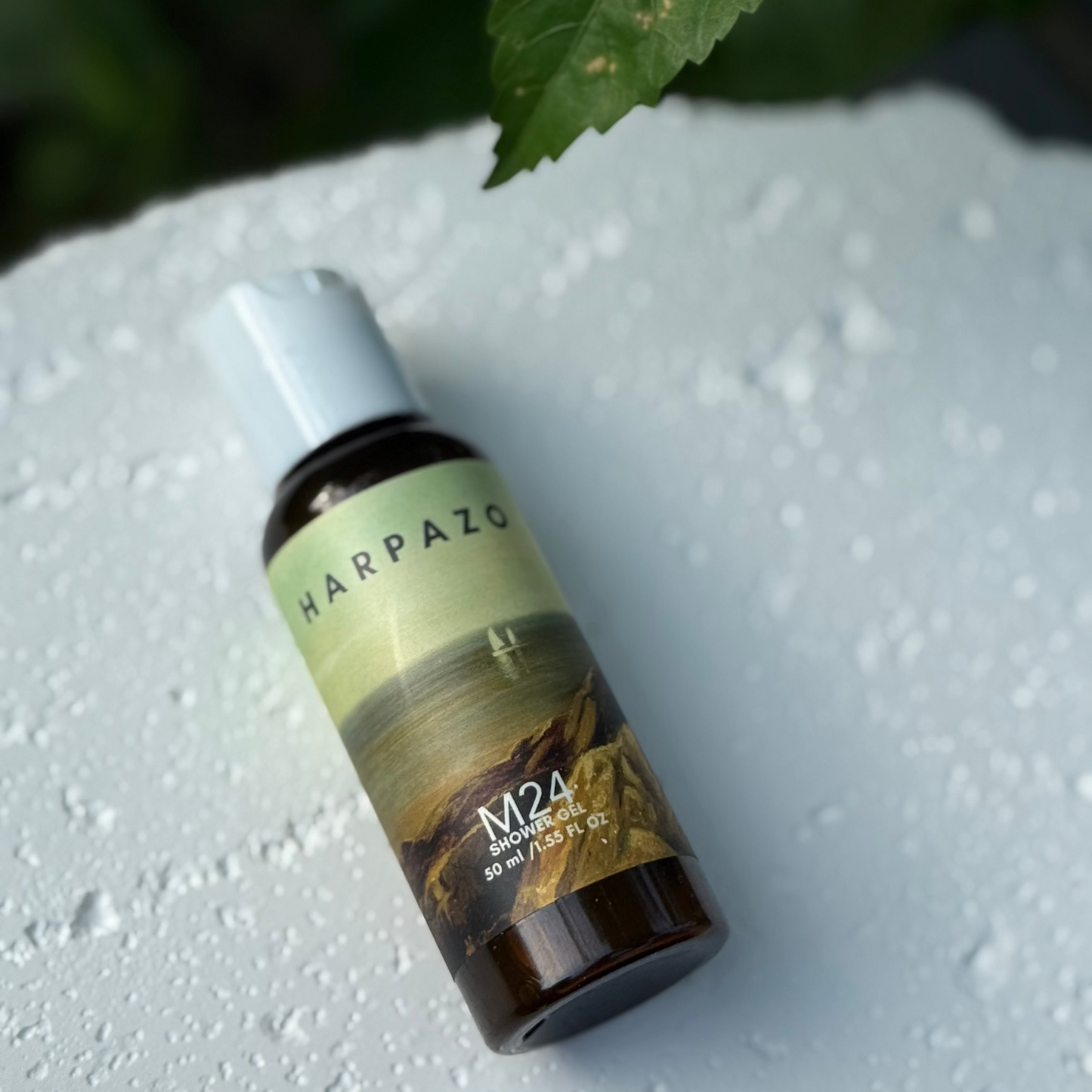 Harpazo M24 shower gel bottle on a textured white surface with a leaf in the background