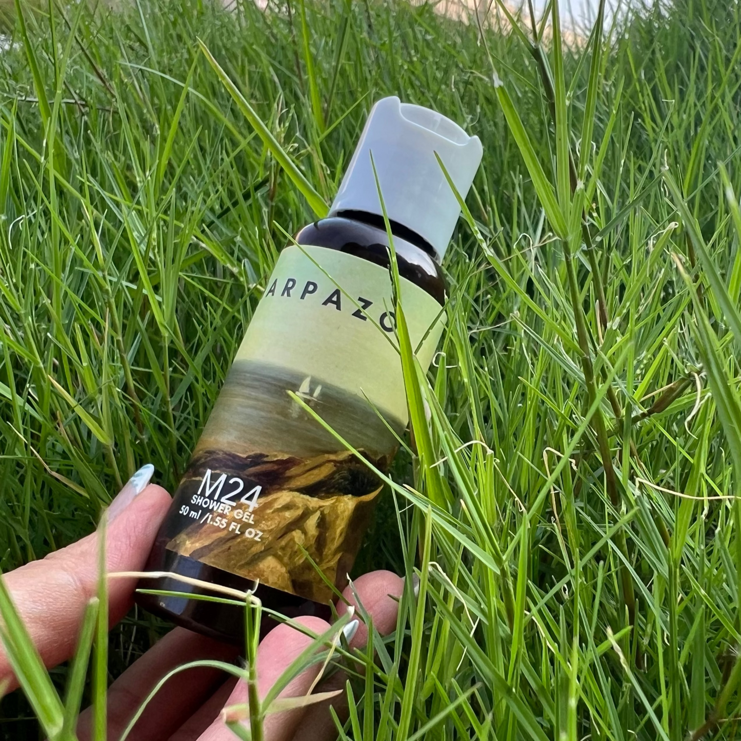 Hand holding a bottle labeled 'Harpazo' in grass