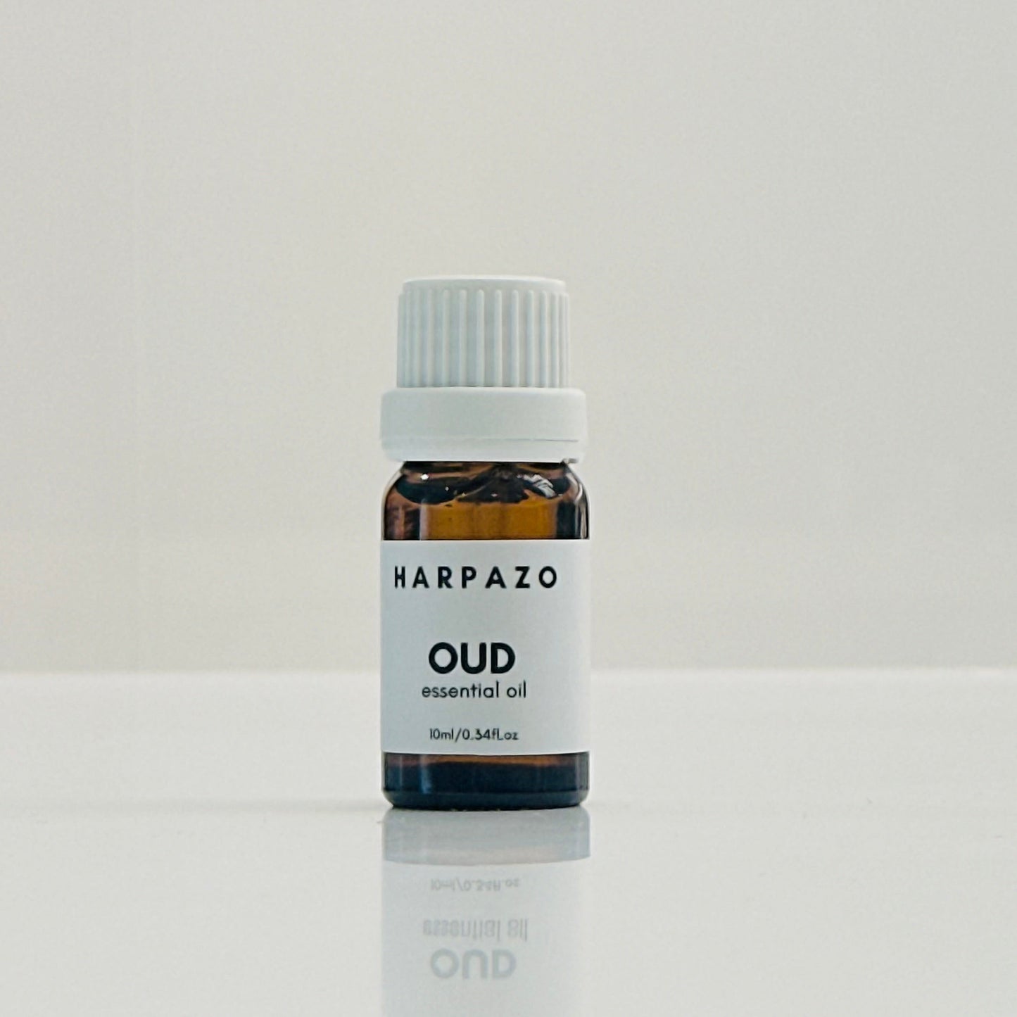 A small bottle labeled 'HARPAZO OUD essential oil' with a capacity of 10ml, placed on a reflective surface against a white background.