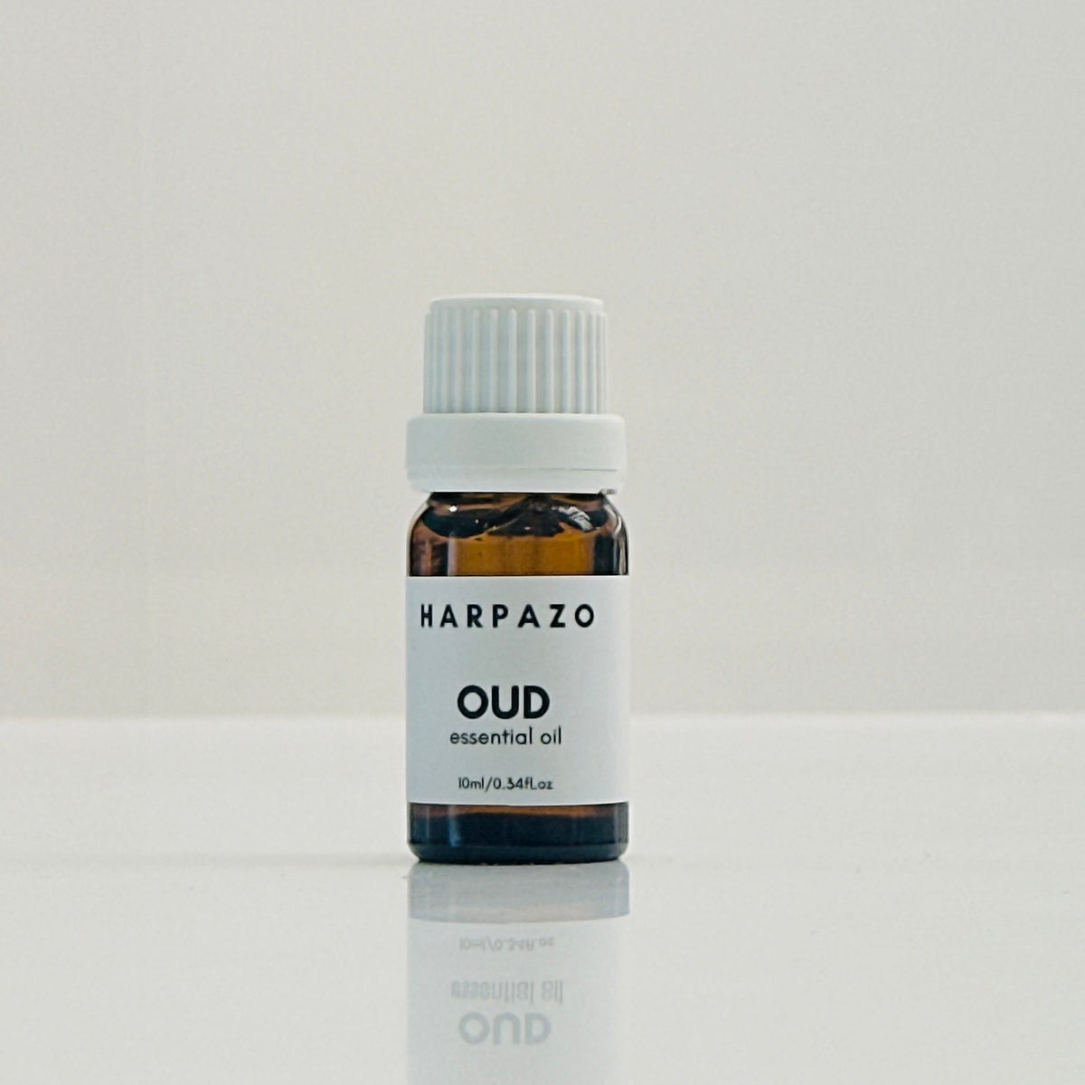 A small bottle labeled 'HARPAZO OUD essential oil' with a capacity of 10ml, placed on a reflective surface against a white background.