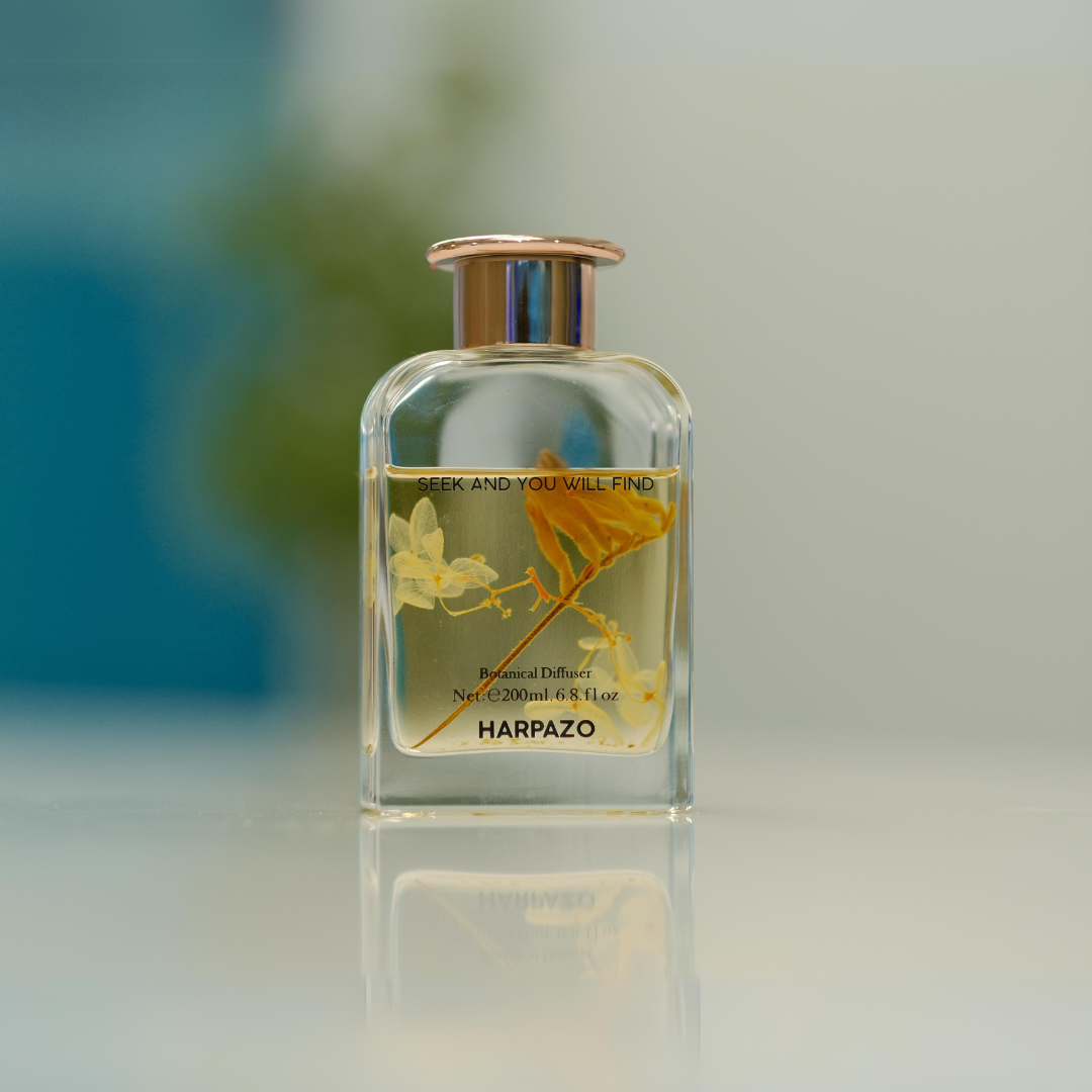 A glass reed diffuser bottle with a clear liquid and orange blossom design, topped with a gold-colored cap.