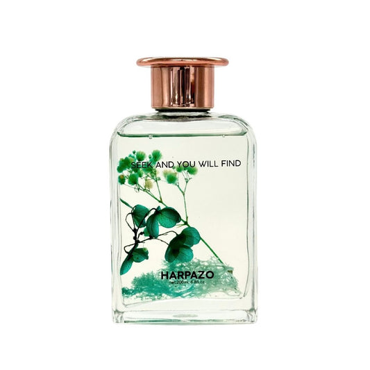 A clear glass reed diffuser bottle with green botanical elements and a rose gold cap, labeled with 'HARPADO' and text encouraging exploration.