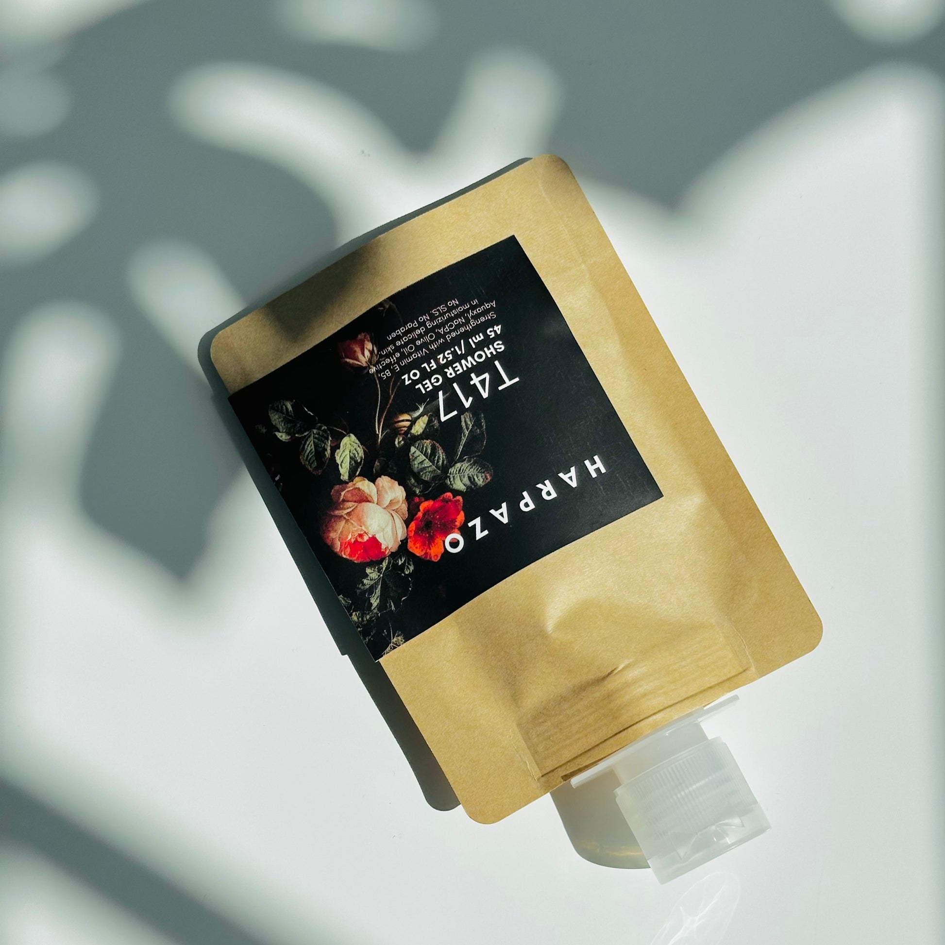 Travel size shower gel bottle with floral design on the label, predominantly in a brown pouch.