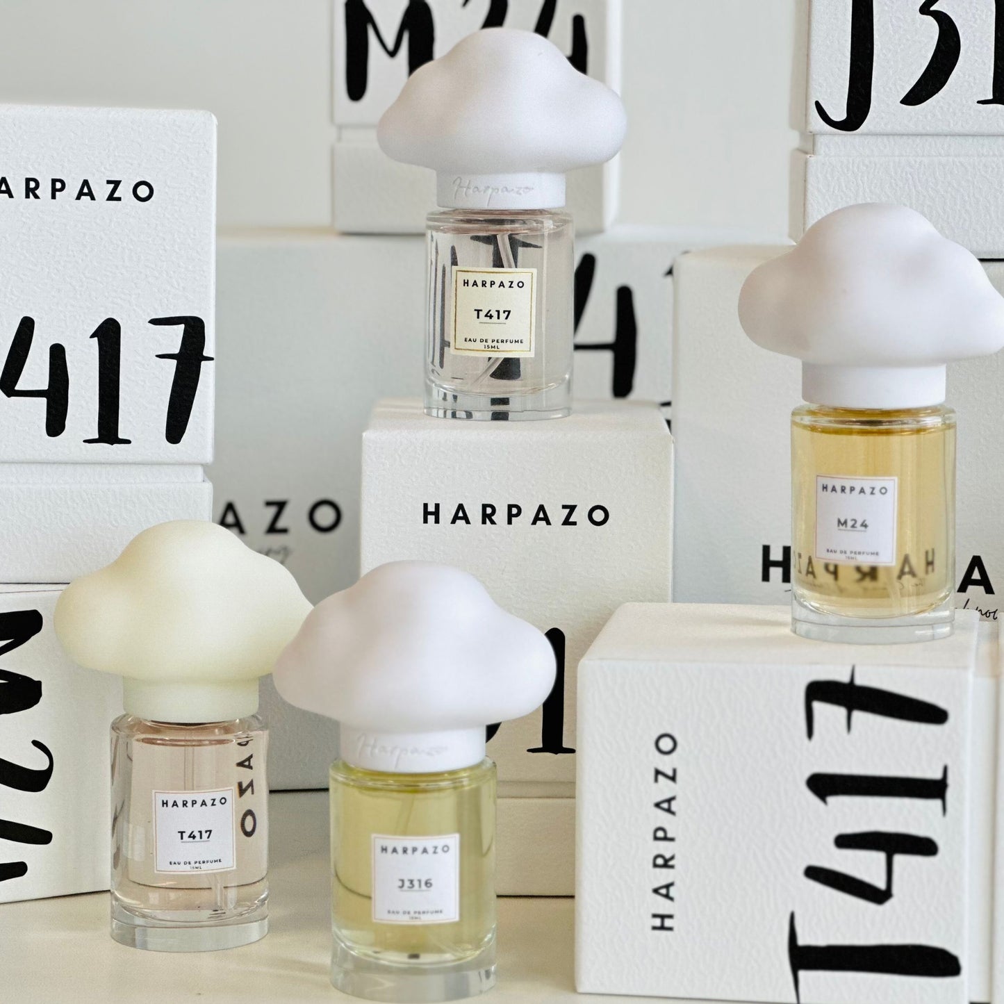 Three glass bottles of perfume with unique cloud-shaped caps, labeled M24, J316, and T417, on a light background.