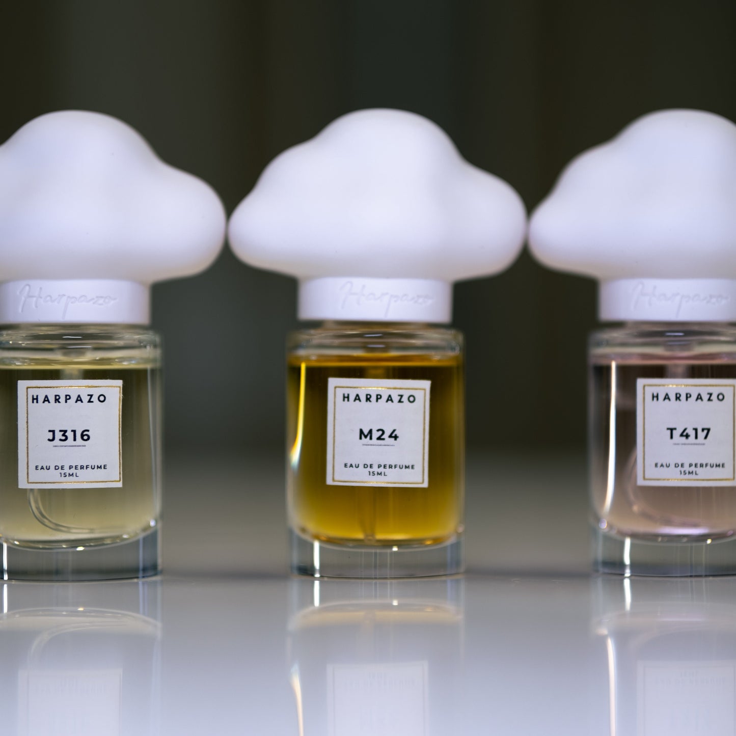 Three glass bottles of perfume with unique cloud-shaped caps, labeled M24, J316, and T417, on a light background.