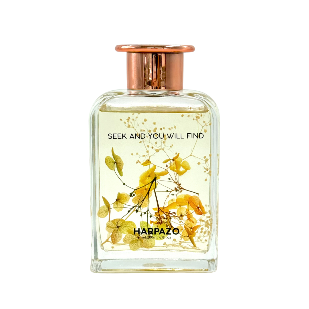 A glass reed diffuser bottle with a copper cap and floral elements inside, labeled 'HARPAZO' with the text 'SEEK AND YOU WILL FIND'.