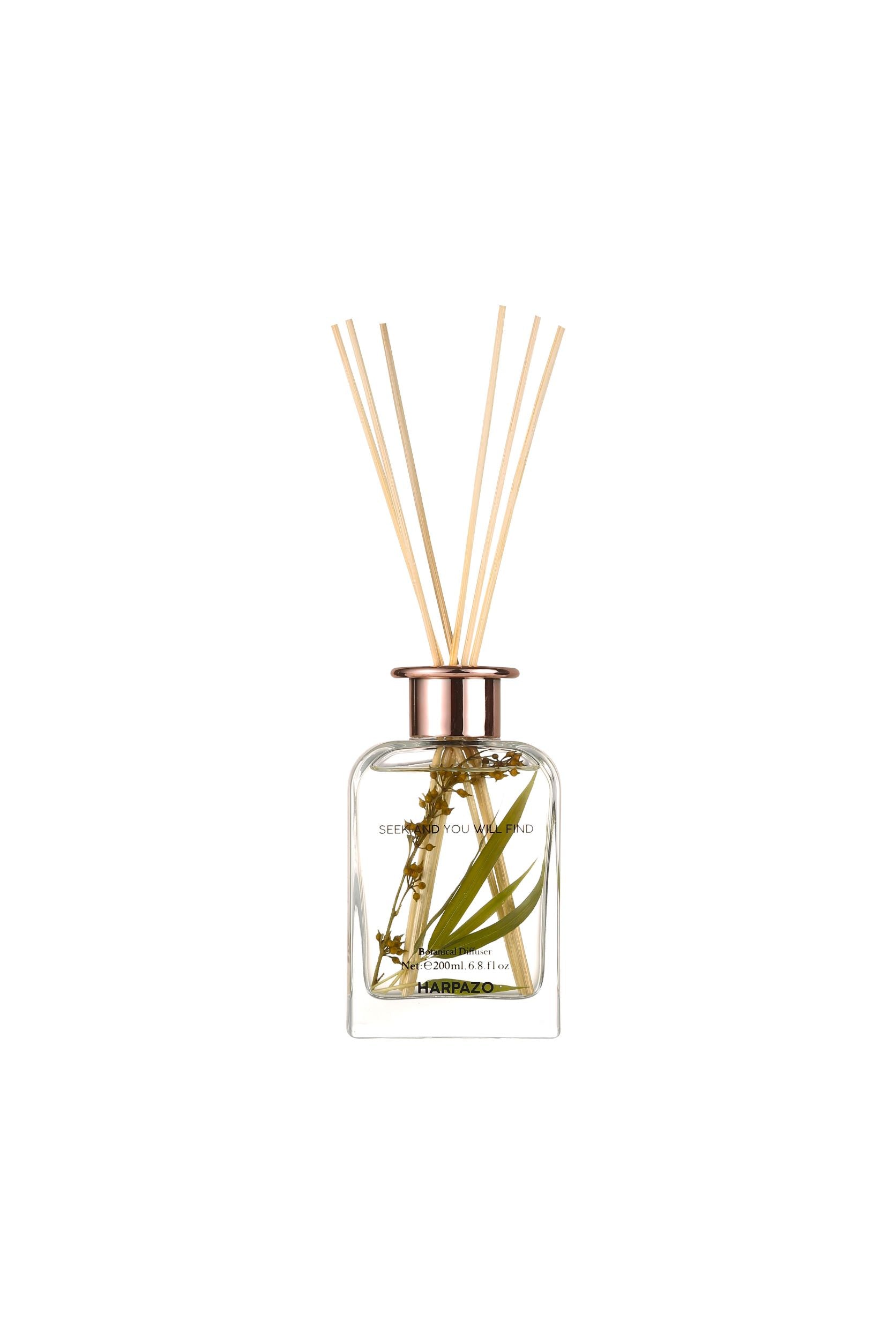 A clear glass bottle with a reed diffuser, containing bamboo and other greenery, with a white background.