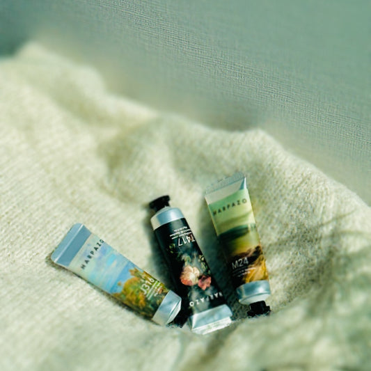 Three travel-size hand cream tubes lying on a textured fabric surface.