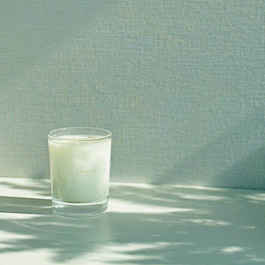 A white aromatic candle in a clear glass holder, placed on a surface with a textured background.
