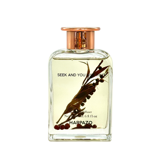 A bottle of fragrance oil labeled 'seek and you will find' with a botanical design, including pine needles and figs, on a white background.