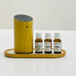 A wooden diffuser machine on a white surface, accompanied by three small bottles of diffusing oil.