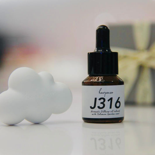 A small bottle labeled J316 Diffuser Oil alongside a white diffusing cloud on a reflective surface.