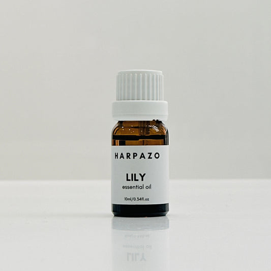 A small bottle labeled 'HARPAZO LILY essential oil' with a white cap, placed on a white surface.