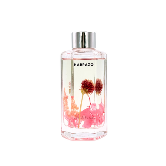 A clear glass reed diffuser bottle with pink floral elements and the brand name 'HARPAZO' visible on the label.