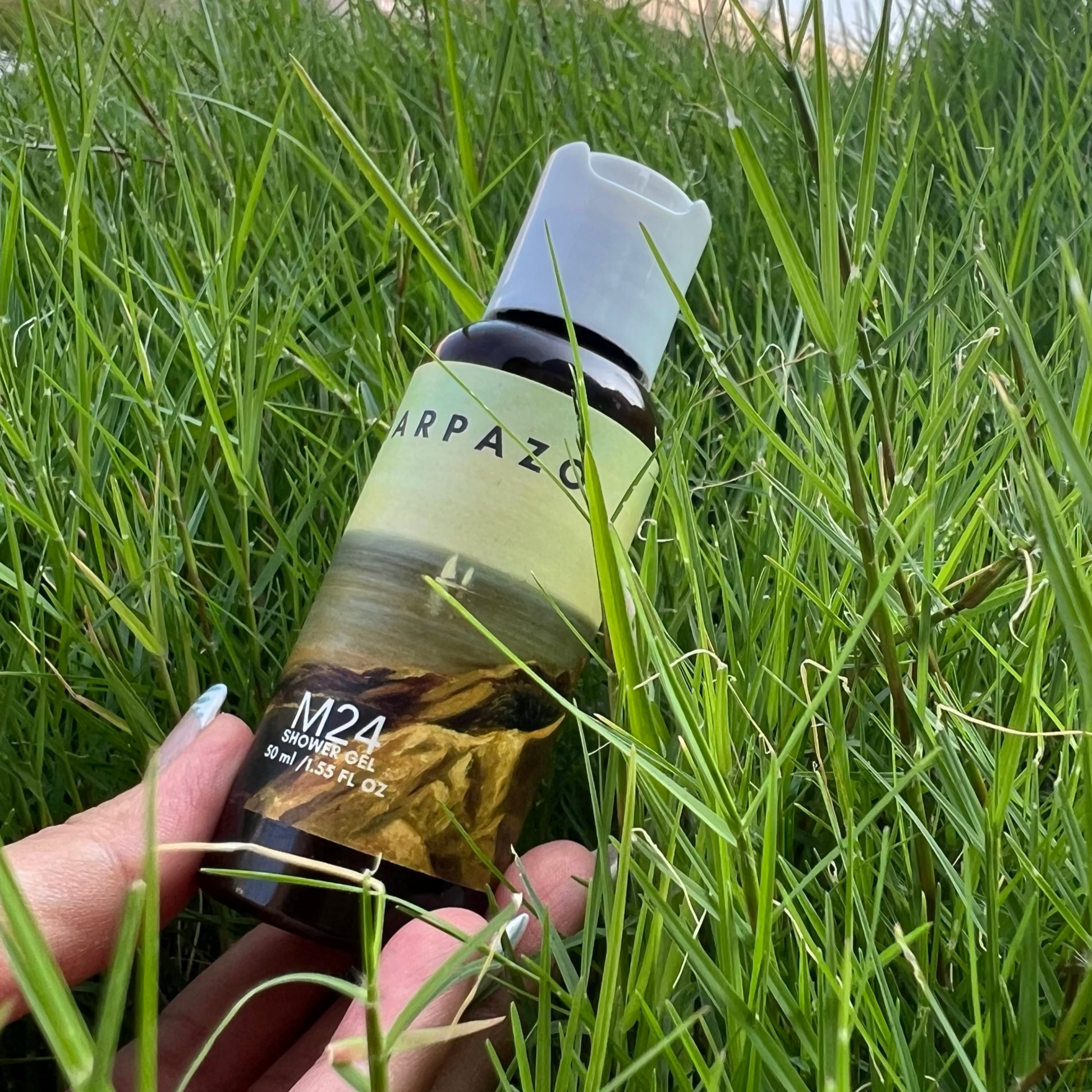 Hand holding a bottle labeled 'Harpazo' in grass
