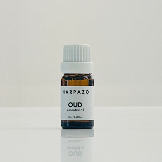 A small bottle labeled 'HARPAZO OUD essential oil' with a capacity of 10ml, placed on a reflective surface against a white background.