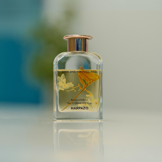 A glass reed diffuser bottle with a clear liquid and orange blossom design, topped with a gold-colored cap.