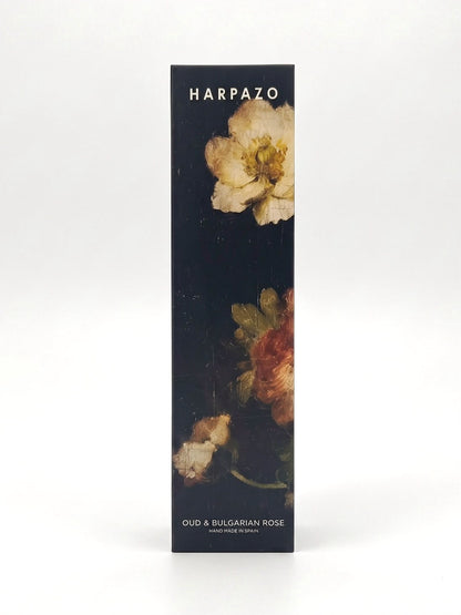 A tall, narrow rectangular product box for Harpazo Oud & Bulgarian Rose, featuring a dark background with classical oil-paint style floral illustrations in cream, red, and green, set against a clean white studio background.