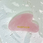Pink gua sha tool with 'Harpazo' branding on a textured white background