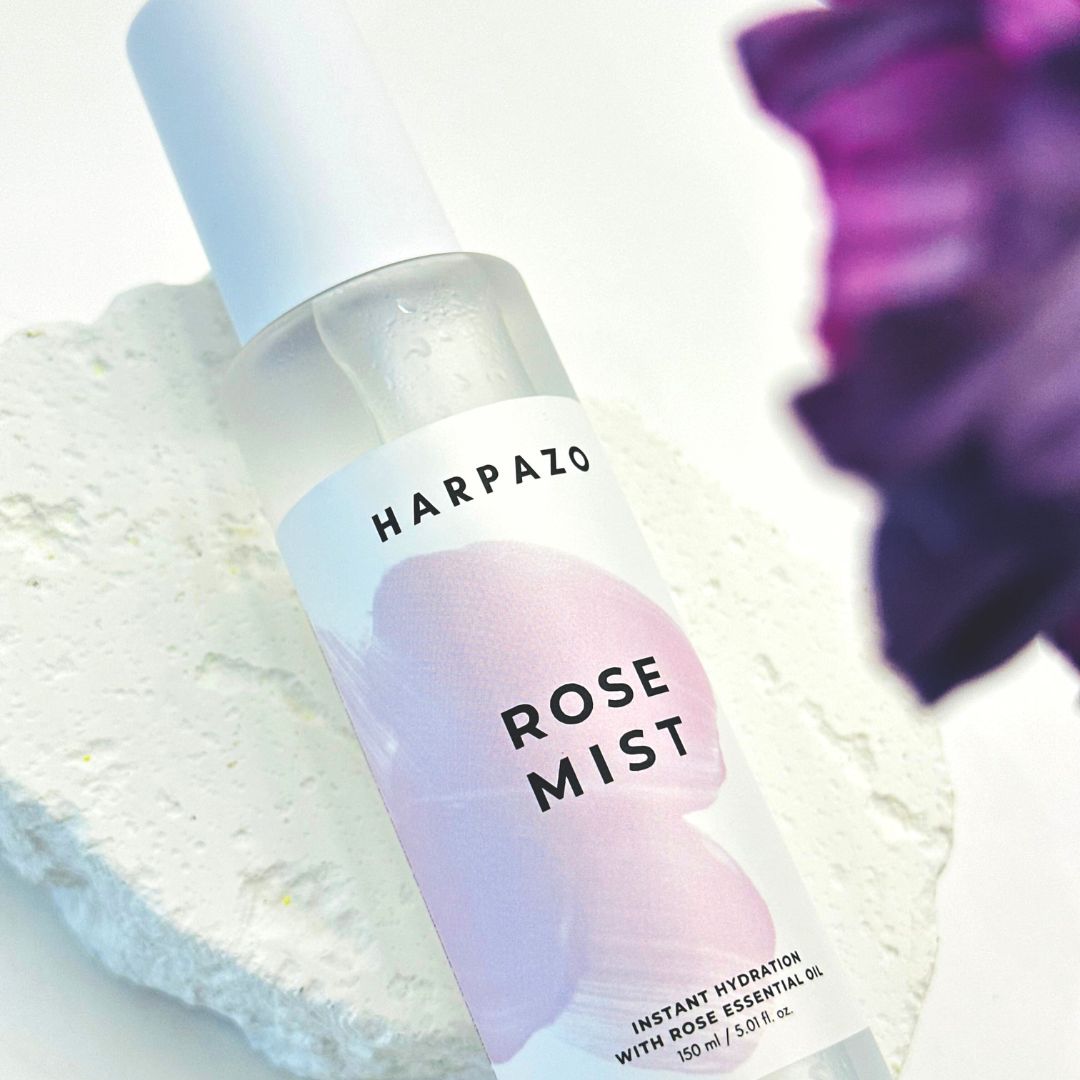 Harpazo Rose Mist bottle on a textured surface with a blurred purple flower in the background