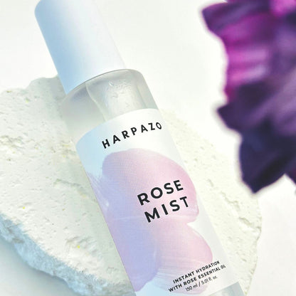 Harpazo Rose Mist bottle on a textured surface with a blurred purple flower in the background
