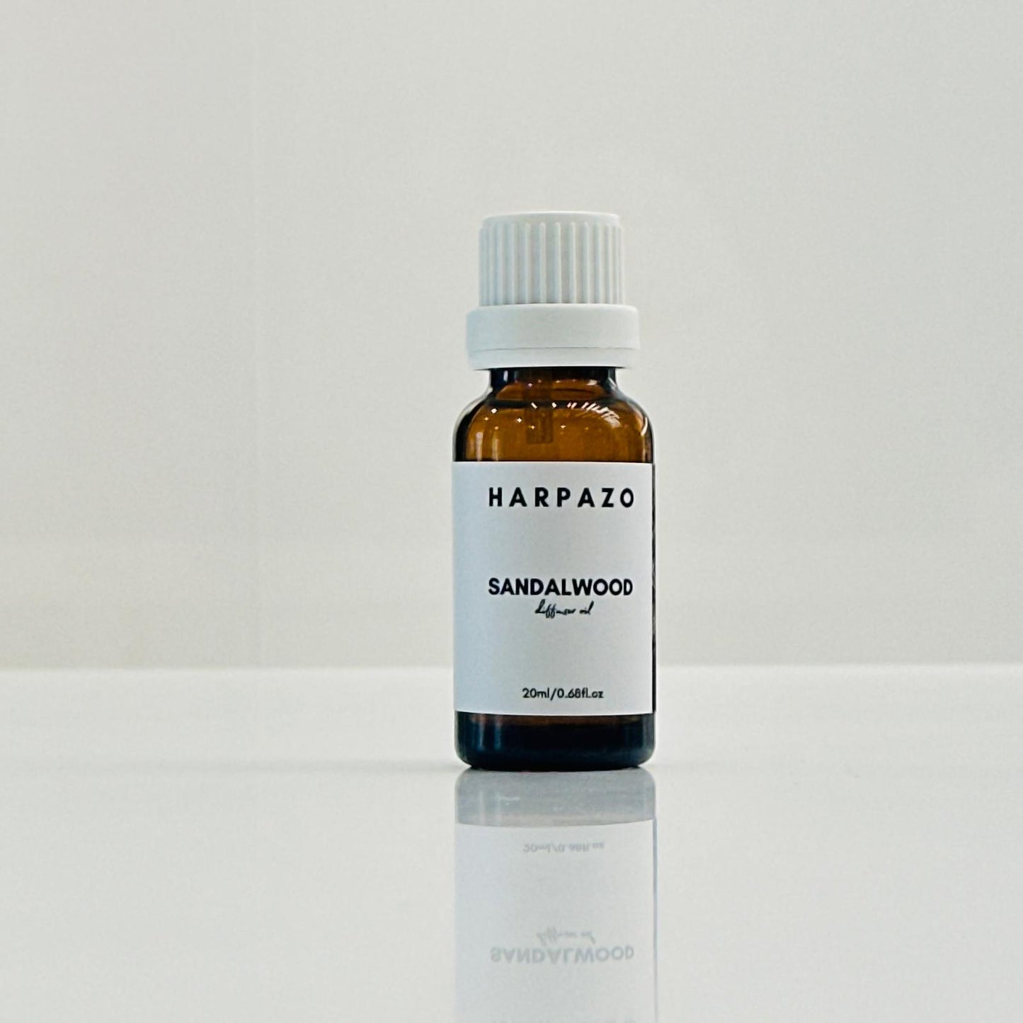 A small bottle labeled 'HARPAZO Sandalwood' diffuser oil, with a white cap, placed on a reflective surface against a white background.