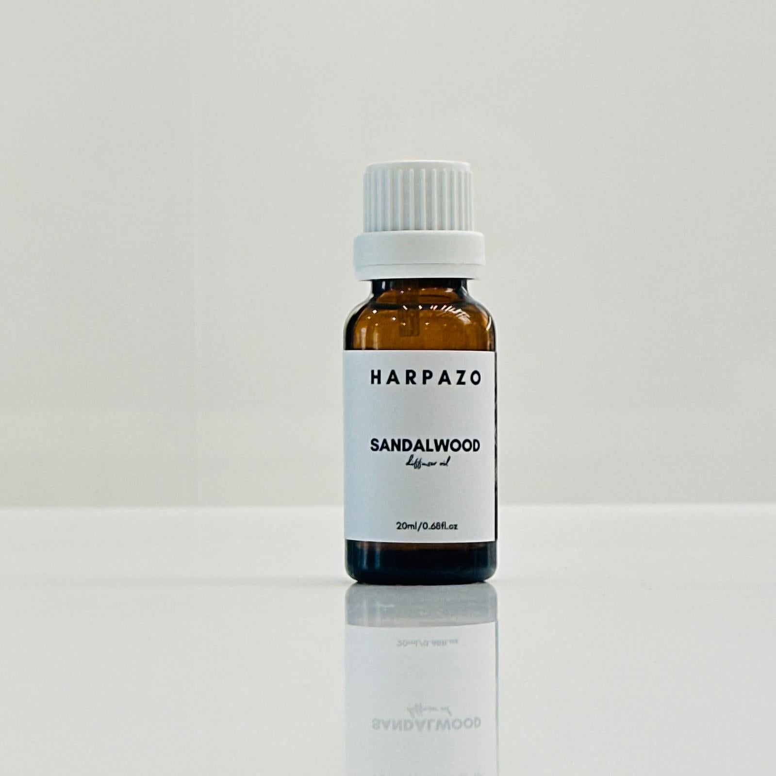 A small bottle labeled 'HARPAZO Sandalwood' diffuser oil, with a white cap, placed on a reflective surface against a white background.