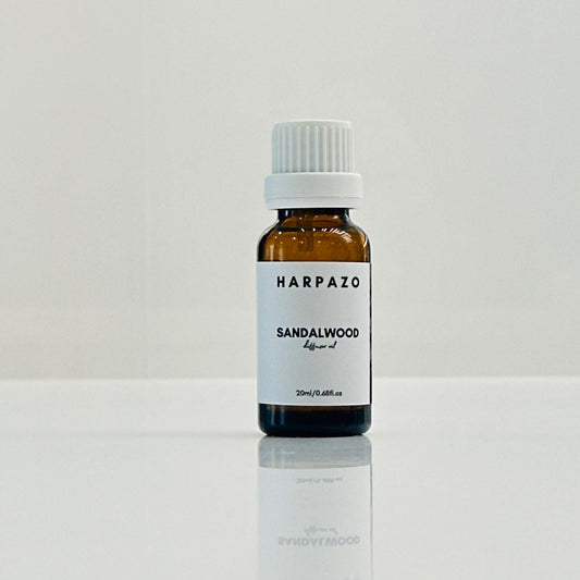 A small bottle labeled 'HARPAZO Sandalwood' diffuser oil, with a white cap, placed on a reflective surface against a white background.