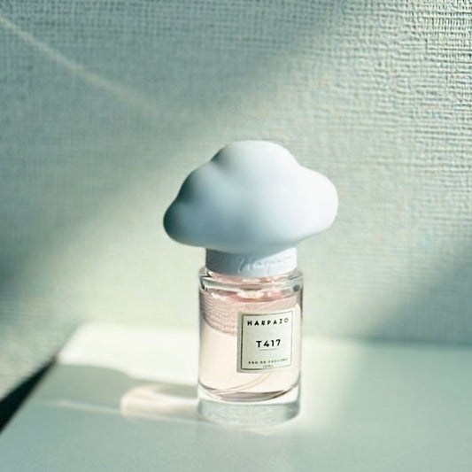 A perfume bottle with a white, cloud-shaped cap, labeled 'T417', placed on a flat surface with a light blue background.