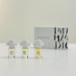 Three glass bottles of perfume with unique cloud-shaped caps, labeled M24, J316, and T417, on a light background.